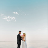 side view of wedding couple standing with bouquet on sandy beach